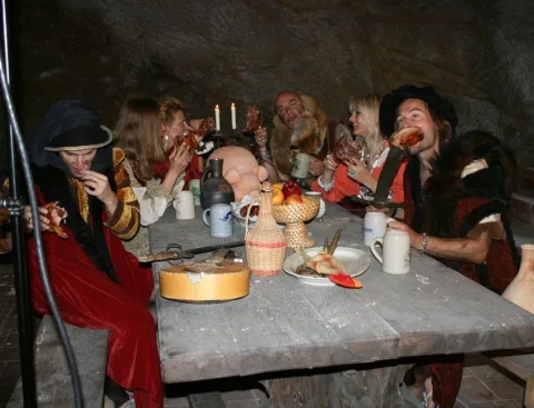 Mehrere Darsteller in historischen Kostümen beim Essen an einer Steintafel