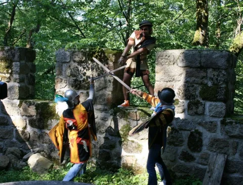 Darsteller mit Speeren auf einer bewachsenen Ruinenmauer