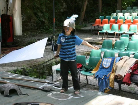 Ein Kind mit Helm auf einer Freilichtbühne mit grünen Stuhlreihen
