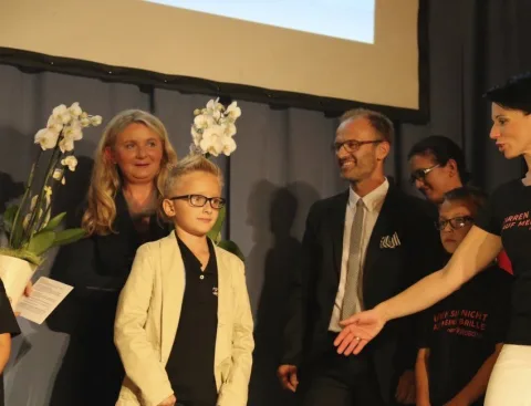 Ein Kind mit Brille auf dem Laufsteg, dahinter Erwachsene