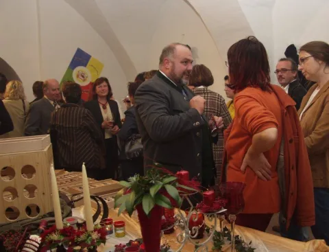 Gäste stehen in einem festlich geschmückten Gewölberaum beisammen, im Vordergrund ein Tisch mit Rosen