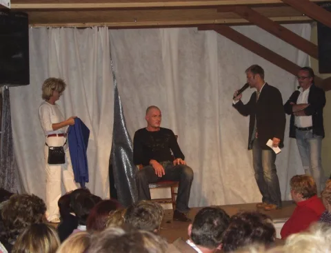 Zwei Personen auf einer kleinen Bühne vor sitzendem Publikum