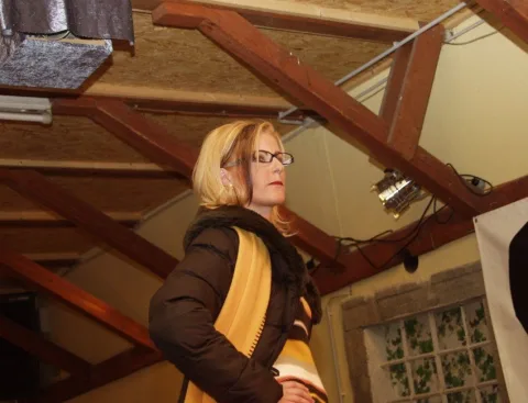Eine Frau mit Brille und Schal geht durch den Raum mit Holzdachstuhl