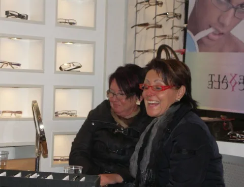 Zwei Frauen mit Brillen lachen vor einer Wand mit ausgestellten Fassungen