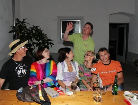 Gäste an einer Biertischgarnitur, einer winkt in die Kamera