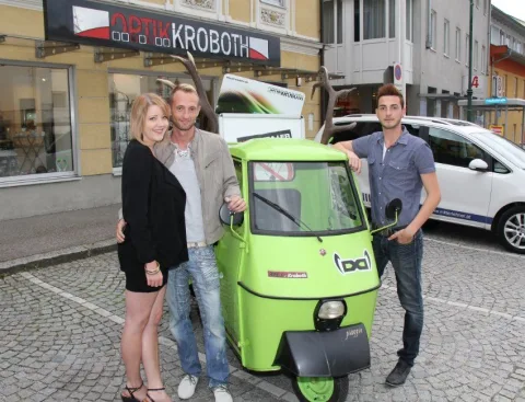 Drei Gäste neben dem grünen Kleintransporter vor dem Geschäft