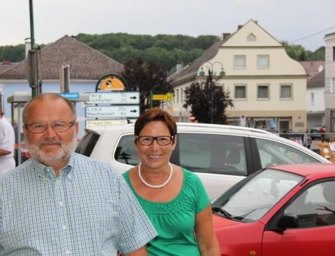 Zwei Gäste vor einem Auto, dahinter der Ortsplatz