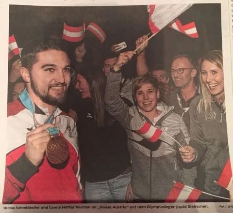 Ein Sportler zeigt seine Medaille, umringt von feiernden Menschen mit Österreichfahnen