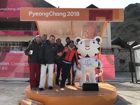 Eine Gruppe posiert auf einer Bühne neben dem Olympia-Maskottchen unter dem Schriftzug PyeongChang 2018
