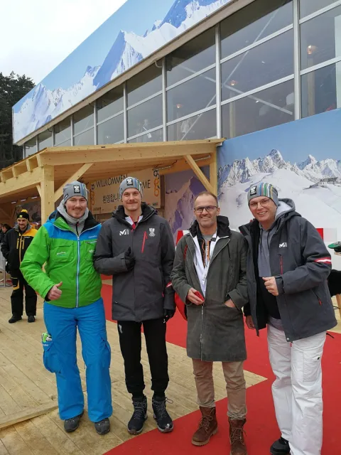 Vier Männer in Winterjacken stehen vor einer Bergkulisse als Fotohintergrund