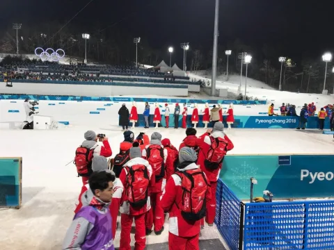 Eine Gruppe in roten Jacken steht abends am beleuchteten Stadionrand