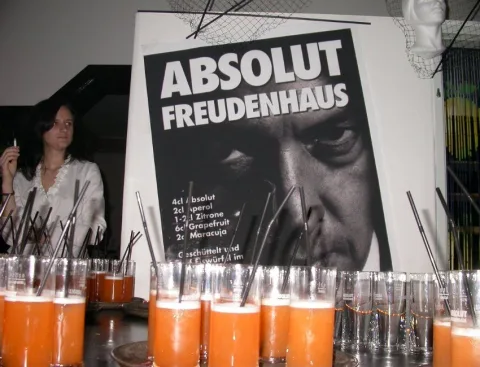 Ein Plakat „Absolut Freudenhaus“ neben Gläsern mit Saft