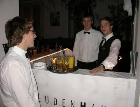 Zwei Kellner hinter der Bar, davor ein Gast
