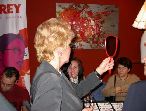 Eine Besucherin mit Handspiegel am Brillentisch