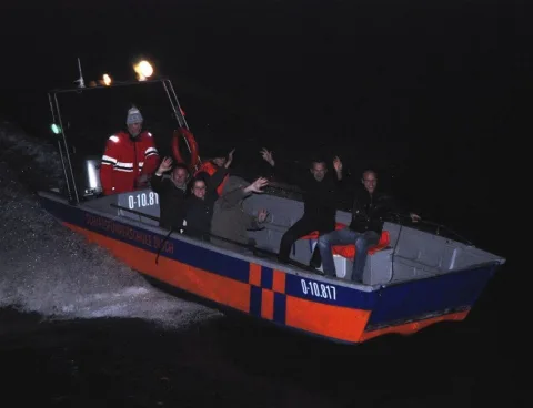 Ein Boot fährt bei Nacht neben dem Schiff