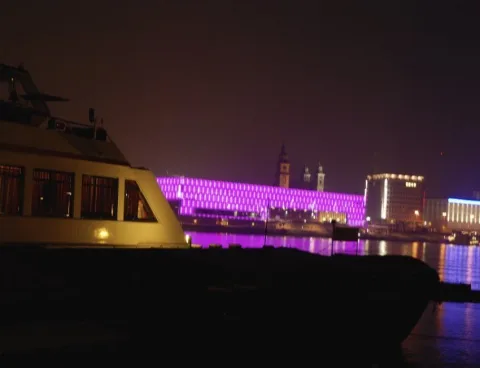 Das Schiff bei Nacht vor einem violett beleuchteten Ufer