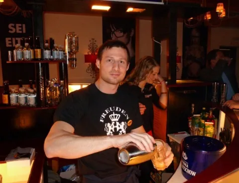 Ein Mann trägt ein T-Shirt mit der Aufschrift „Verboten xxx“ und gießt ein Getränk in ein Glas