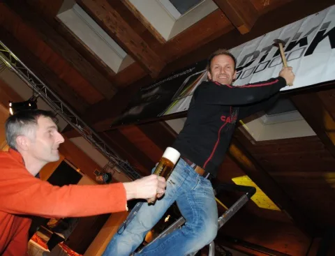 Zwei Männer stehen auf einer Leiter und einer hält ein Bier