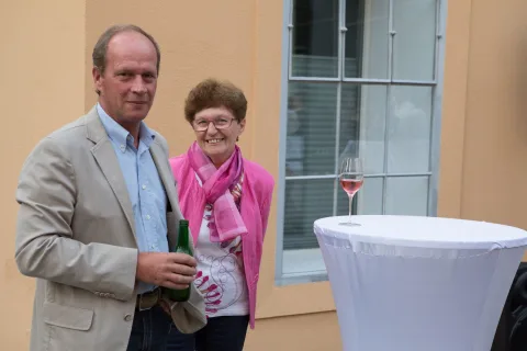 Ein Mann und eine Frau stehen mit einem Glas Wein neben einem Tisch.