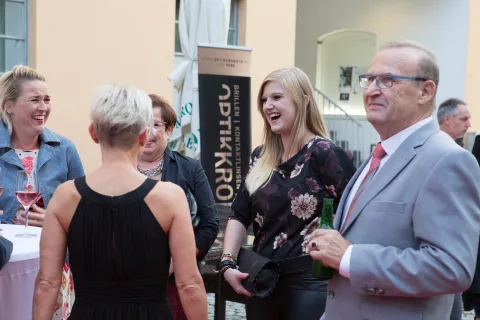 Eine Gruppe von Menschen steht vor einem Schild mit der Aufschrift „Optikkro“.