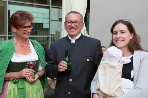 Ein Mann hält eine Flasche Wein und eine Frau ein Baby.