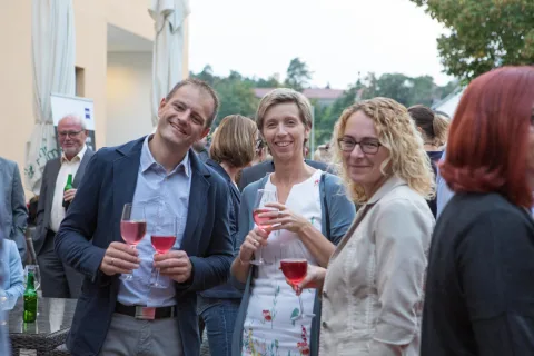 Eine Gruppe von Menschen steht mit Weingläsern in den Händen nebeneinander.