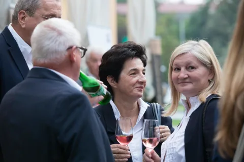 Eine Gruppe von Leuten steht herum, unterhält sich und trinkt Wein.