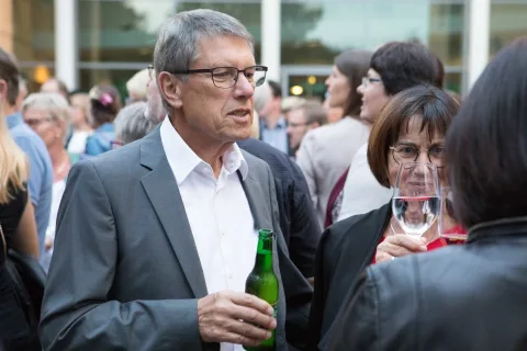 Ein Mann im Anzug hält eine Flasche Bier und ein Glas Wein in der Hand.