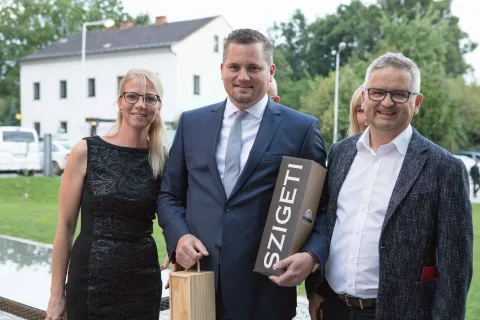 Ein Mann im Anzug hält ein Schild mit der Aufschrift „Szigeti“