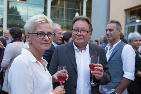 Ein Mann und eine Frau stehen nebeneinander und halten Weingläser in der Hand.