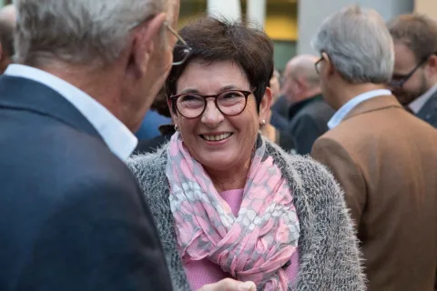 Eine Frau mit Brille und rosa Schal spricht mit einem Mann im Anzug.