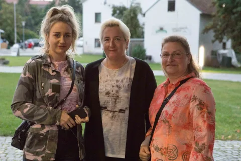 Drei Frauen posieren für ein Foto vor einem weißen Gebäude.