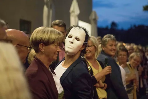 Ein Mann mit einer weißen Maske steht in einer Menschenmenge.
