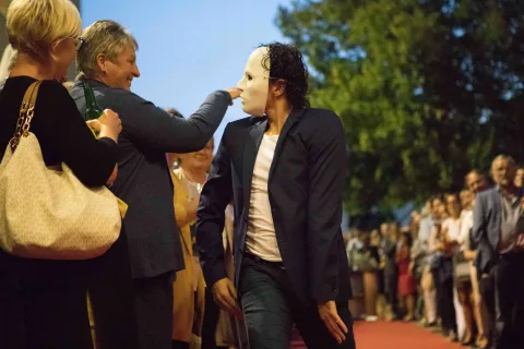 Ein Mann mit einer Maske steht vor einer Menschenmenge.