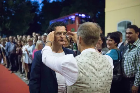 Ein Mann rückt vor einer Menschenmenge die Brille eines anderen Mannes zurecht.