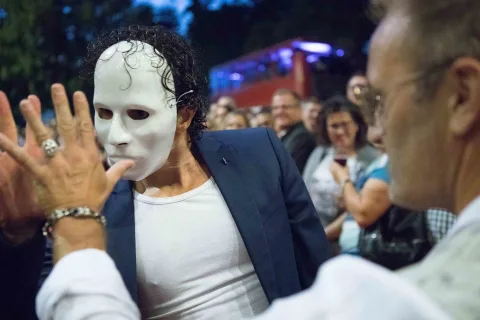 Ein Mann mit einer weißen Maske steht neben einem anderen Mann.