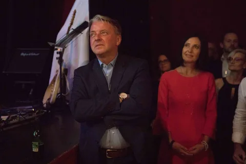 Ein Mann im Anzug und eine Frau im roten Kleid stehen vor einem Mikrofon.