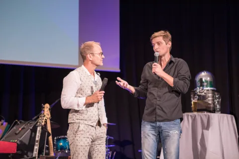 Zwei Männer stehen auf einer Bühne und sprechen in Mikrofone.