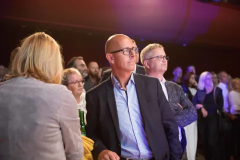 Ein Mann in Anzug und Brille steht vor einer Menschenmenge.