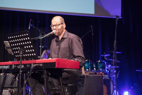 Ein Mann singt in ein Mikrofon, während er auf einer Bühne Keyboard spielt.