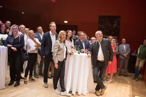 Eine Gruppe von Menschen steht in einem Raum um Tische herum.