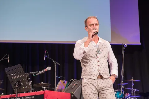 Ein Mann steht auf einer Bühne und hält ein Mikrofon.