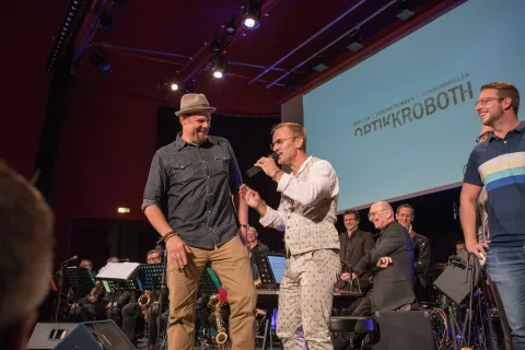 Eine Gruppe von Männern steht auf einer Bühne und unterhält sich miteinander.