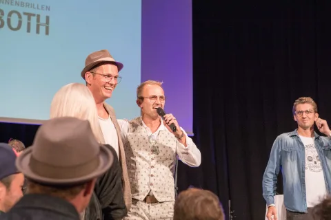 Eine Gruppe Männer steht auf einer Bühne und spricht in Mikrofone.