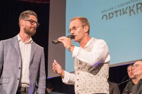 Ein Mann mit Brille spricht in ein Mikrofon, während er neben einem anderen Mann steht