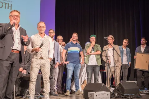 Eine Gruppe von Männern steht mit Mikrofonen in der Hand auf einer Bühne.