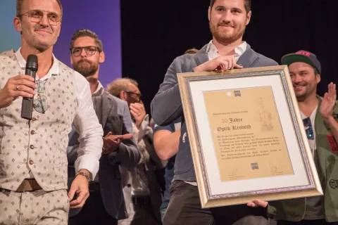 Ein Mann hält vor einer Gruppe von Männern ein gerahmtes Zertifikat in der Hand.