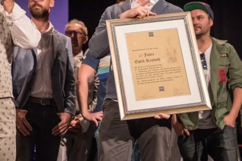 Eine Gruppe von Menschen steht um einen Mann herum, der ein gerahmtes Zertifikat hält