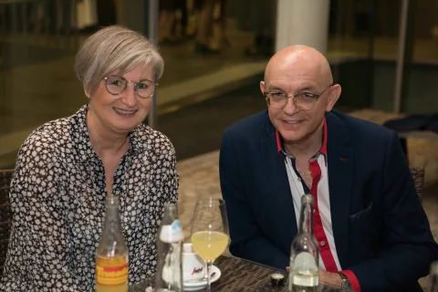 Ein Mann und eine Frau sitzen mit Weingläsern an einem Tisch.