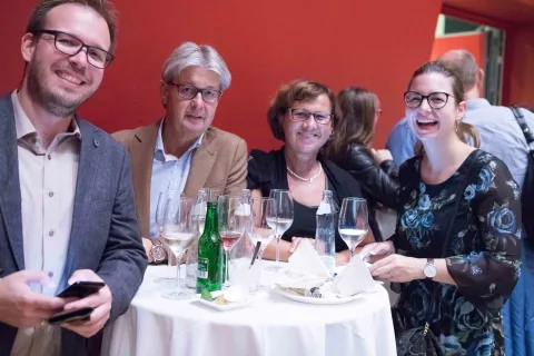 Eine Gruppe von Menschen sitzt mit Weingläsern an einem Tisch.